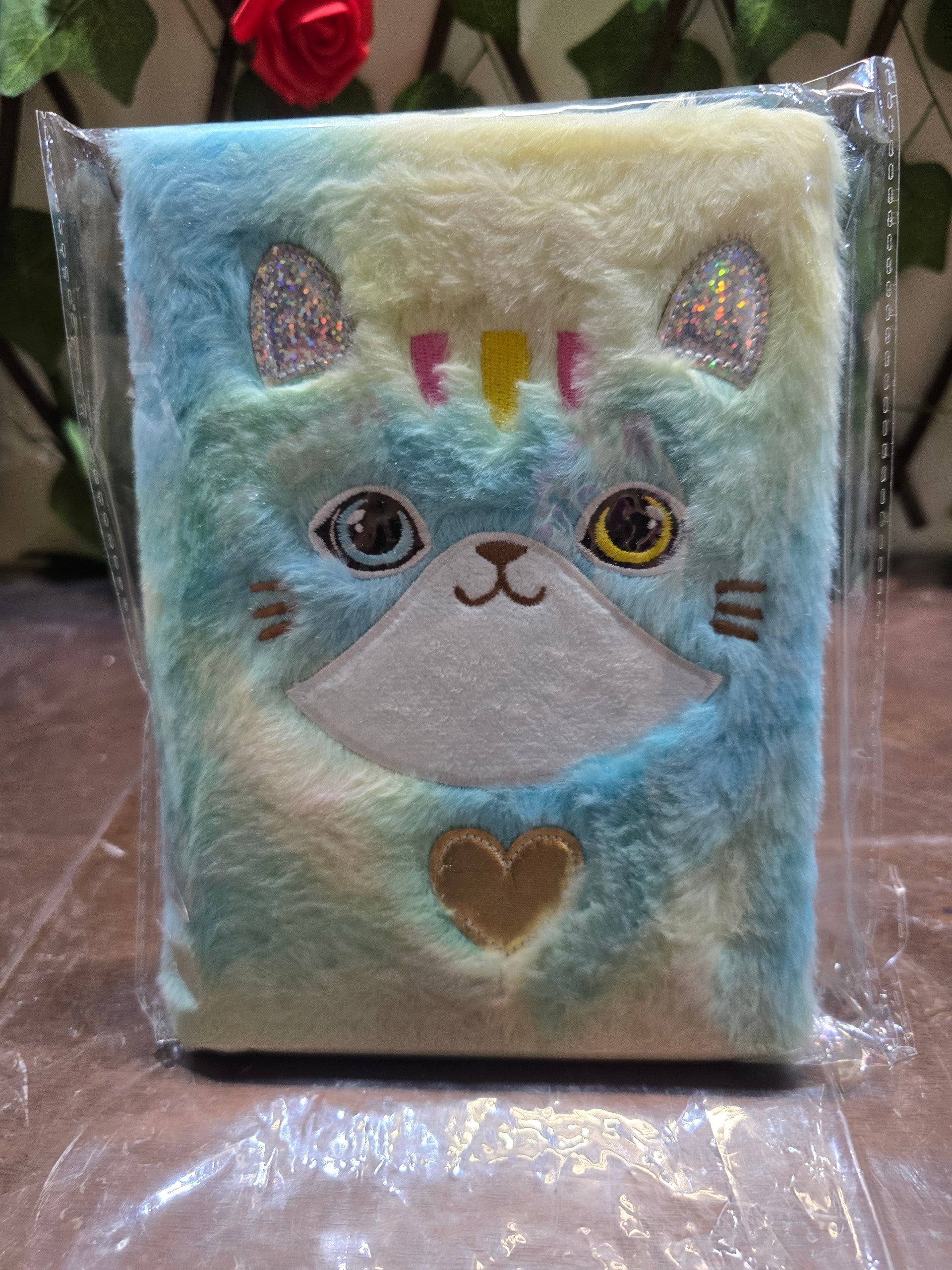BioCode plush cat notebook with multi-coloured faux fur, shimmering ears, and a gold heart accent in plastic wrap