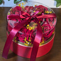 BioCode preserved red roses in a circular gift box with a clear lid, yellow filler flowers, and a satin ribbon bow.