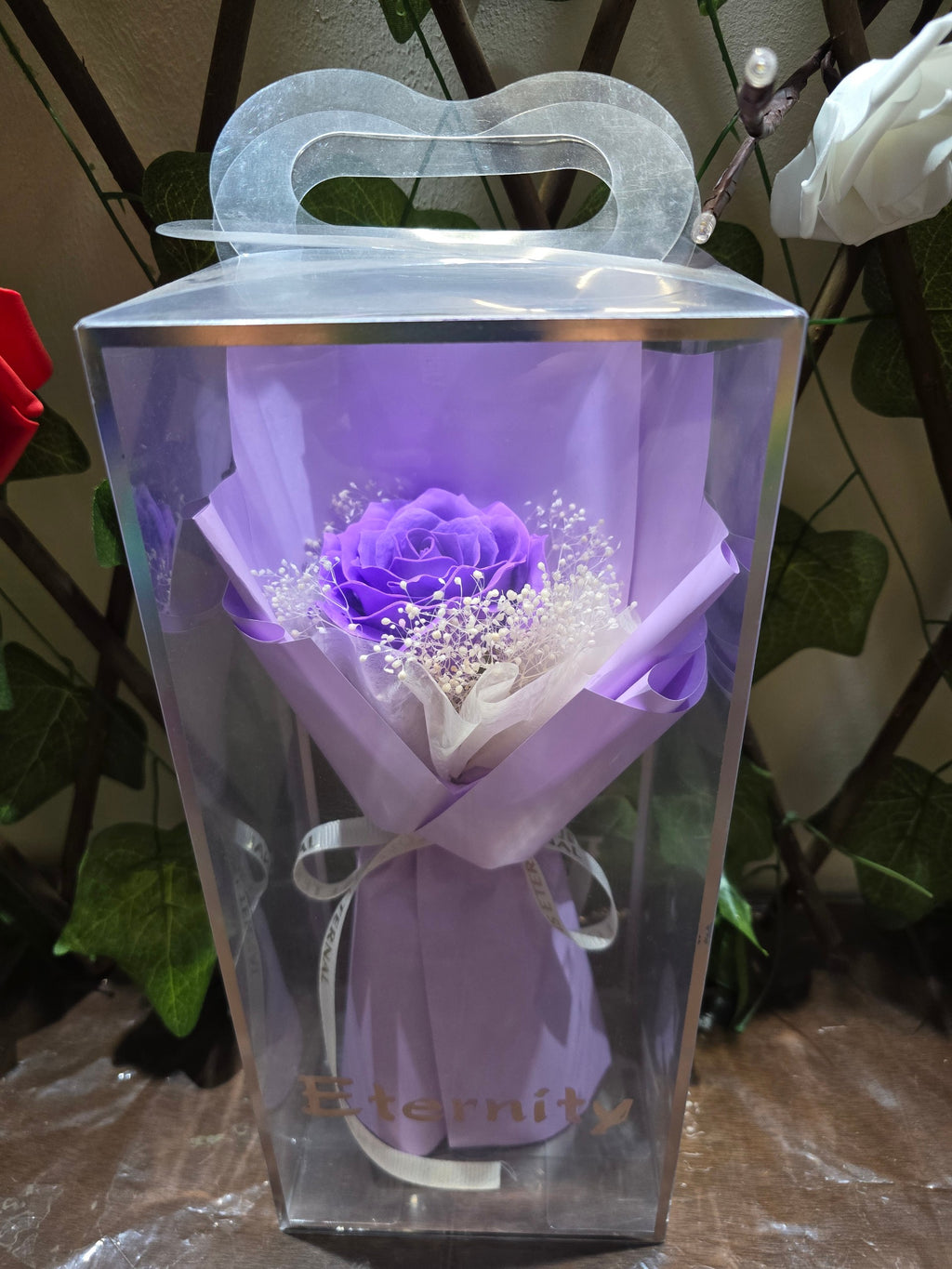 BioCode Eternity single purple artificial rose bouquet with baby's breath in a clear presentation gift box.