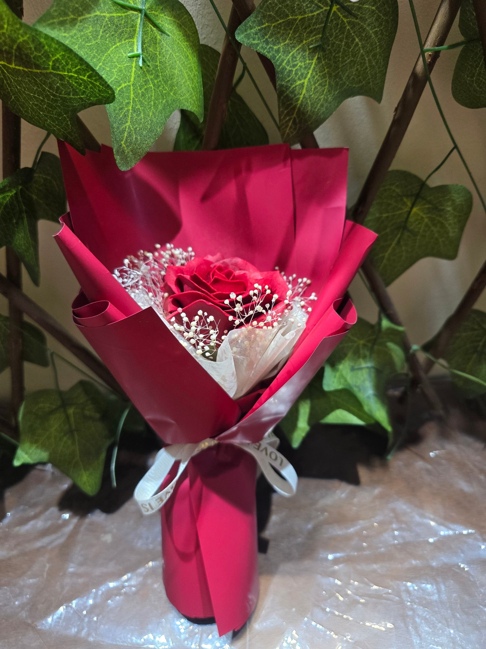 BioCode red artificial eternity rose bouquet wrapped in red paper with white ribbon and baby's breath accents