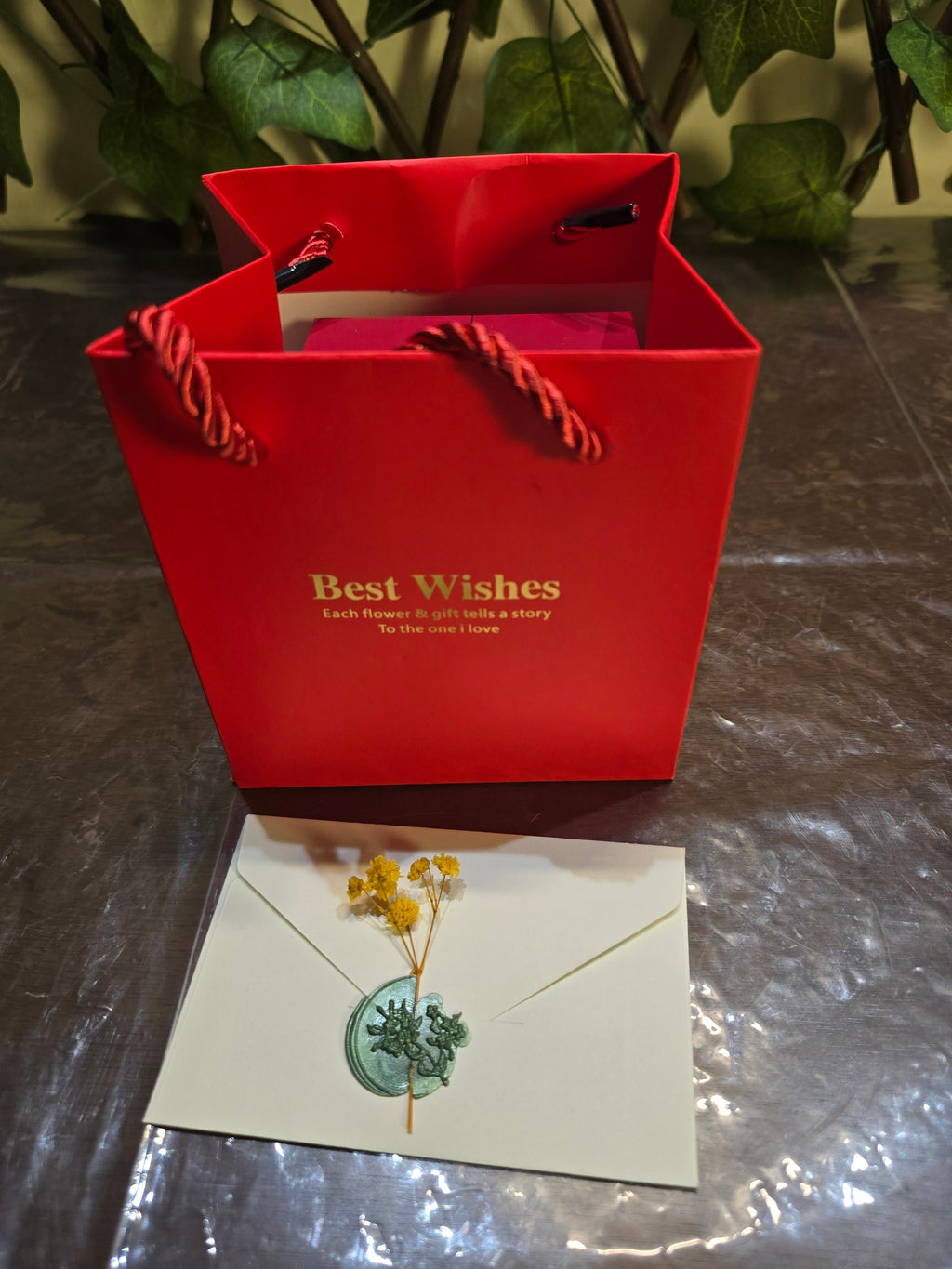 BioCode red gift bag with gold text and a cream envelope sealed with a green wax stamp and dried yellow flowers