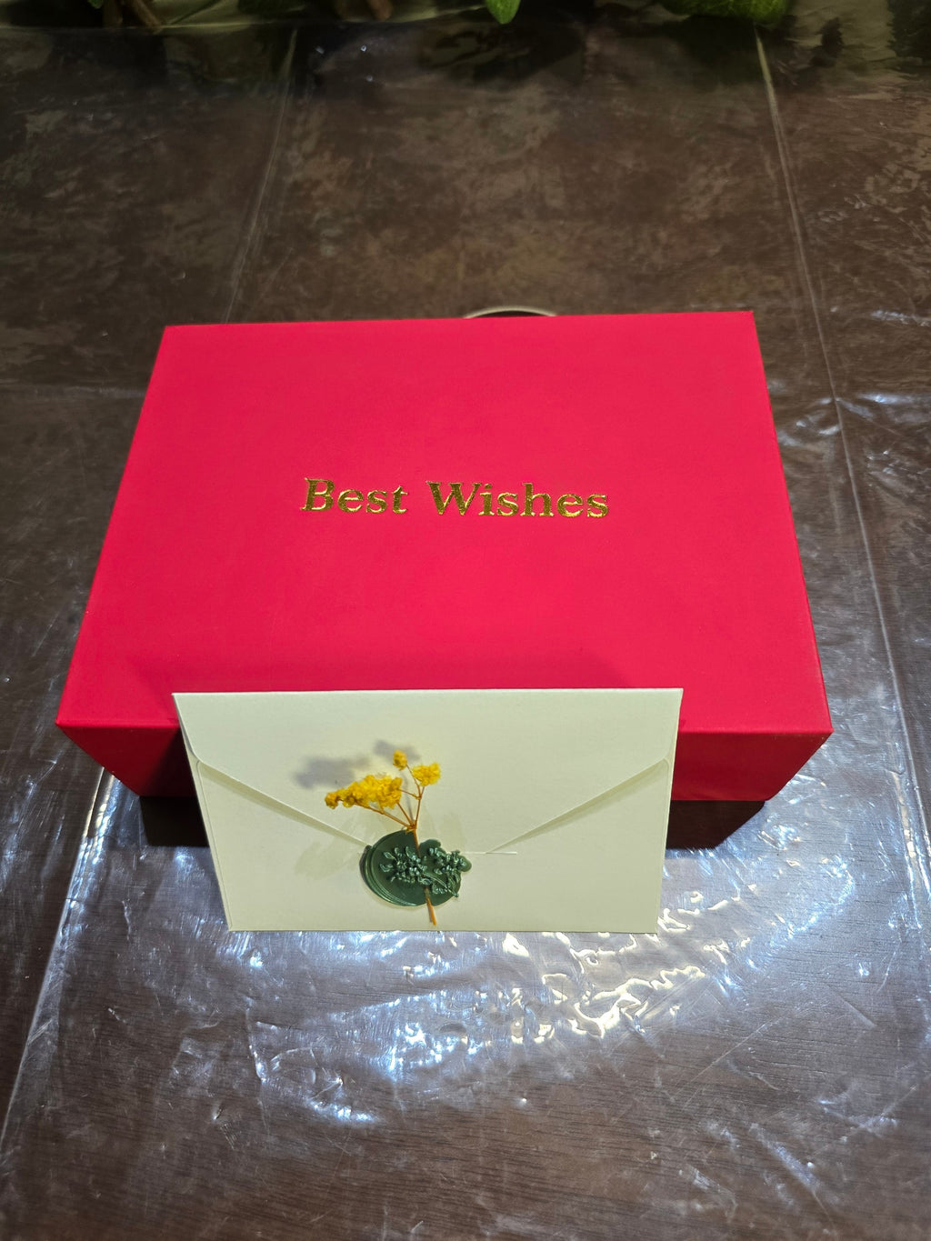 BioCode red gift box with gold Best Wishes text and a cream envelope featuring a wax seal and dried flowers