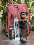 BioCode deep red laptop backpack with a sports water bottle and beaded bracelets in front of a green leaf backdrop.