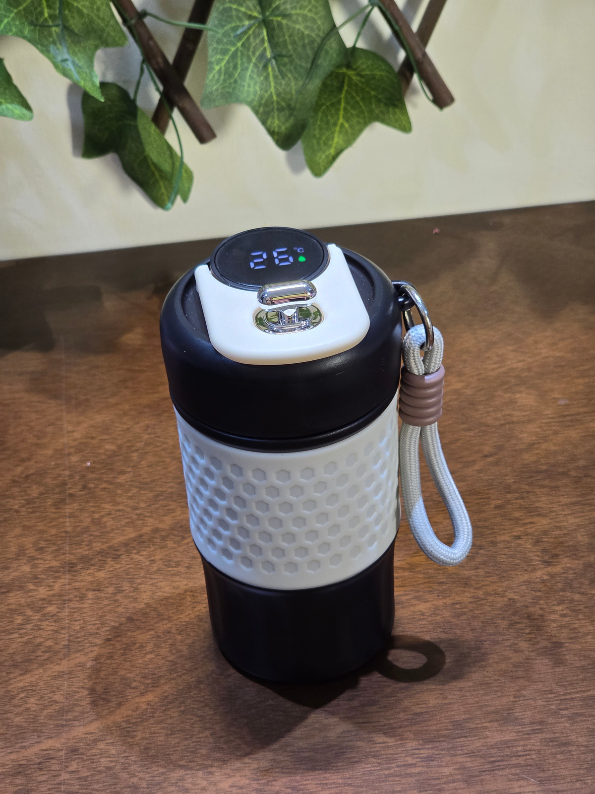BioCode smart thermal mug with LED temperature display, honeycomb grip, and carry strap on a wooden surface