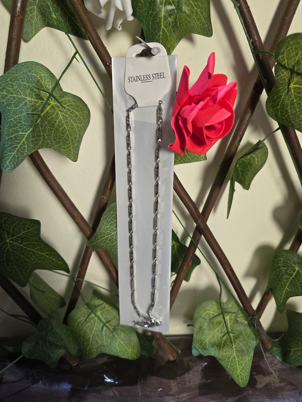 BioCode stainless steel chain necklace on a display card, set against a background of green ivy and a red rose.