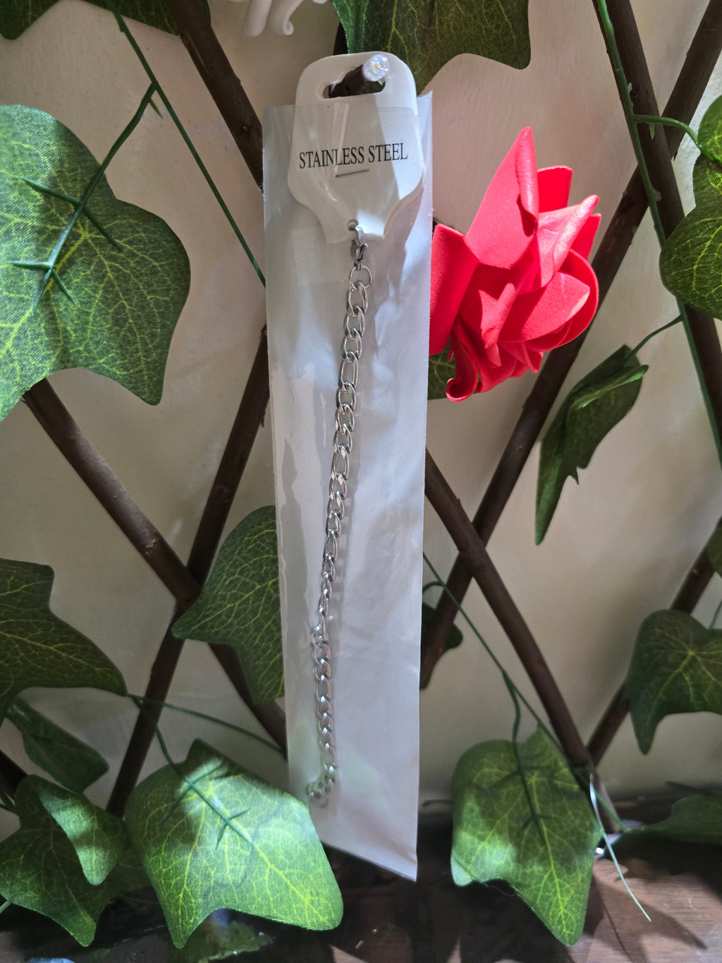 BioCode stainless steel chain necklace in protective packaging hanging against a decorative ivy and red rose backdrop