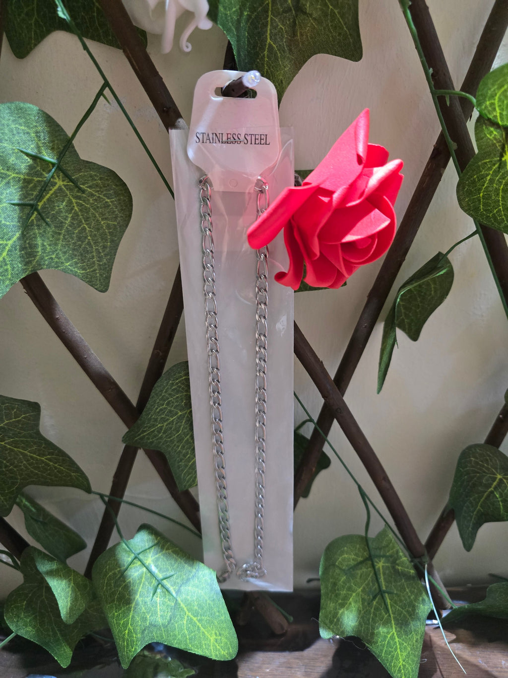 BioCode stainless steel chain necklace in clear plastic packaging with a decorative red rose against a trellis background