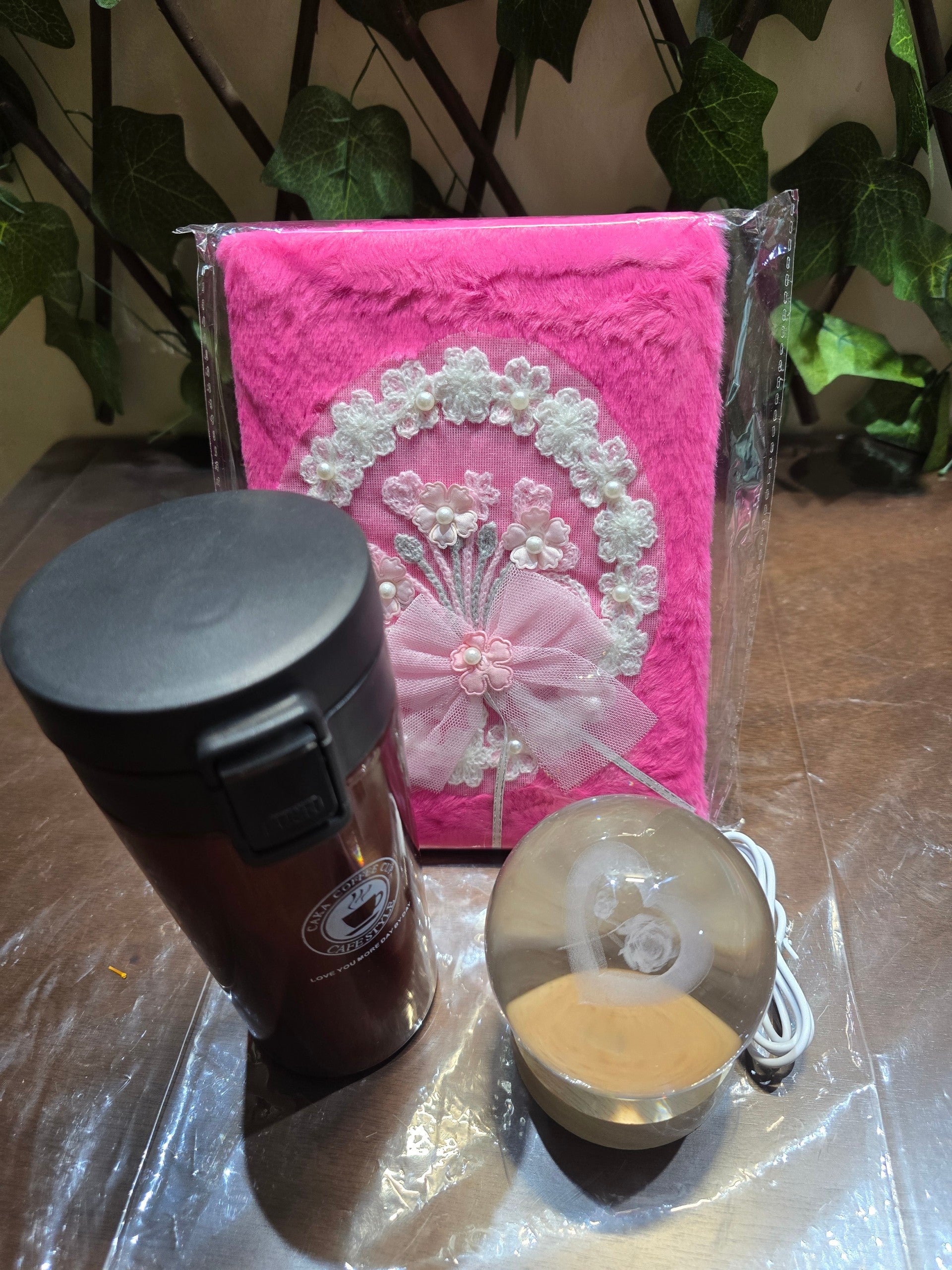 BioCode gift set featuring a pink plush notebook with lace flowers, a dark travel mug, and a crystal ball night light.