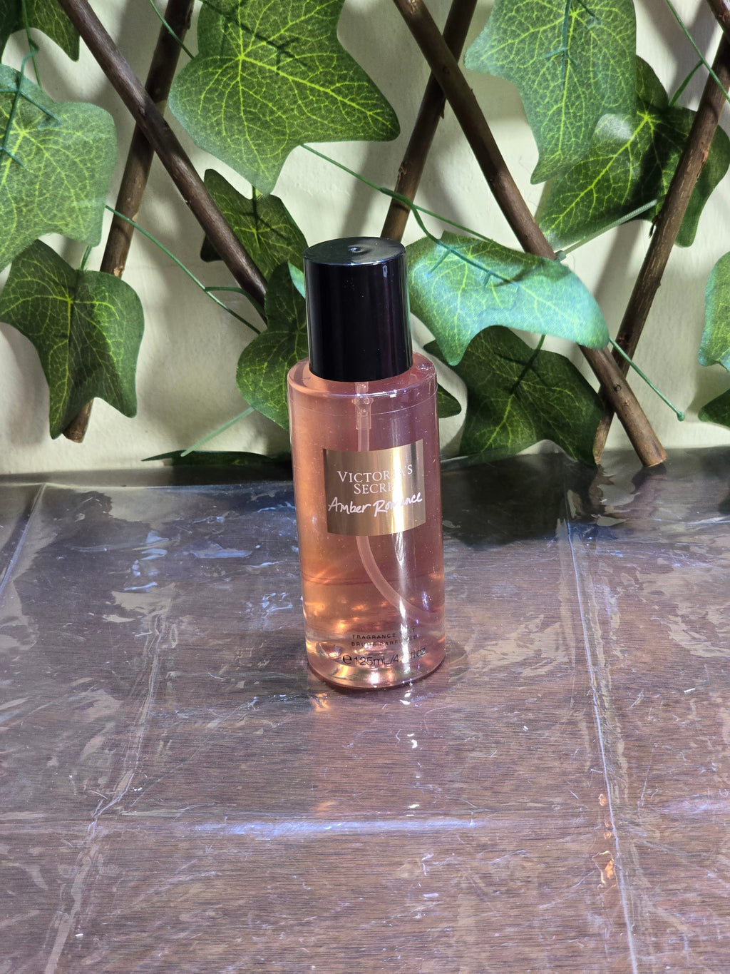BioCode Victoria's Secret Amber Romance fragrance mist in a clear bottle with a black cap against a leafy background
