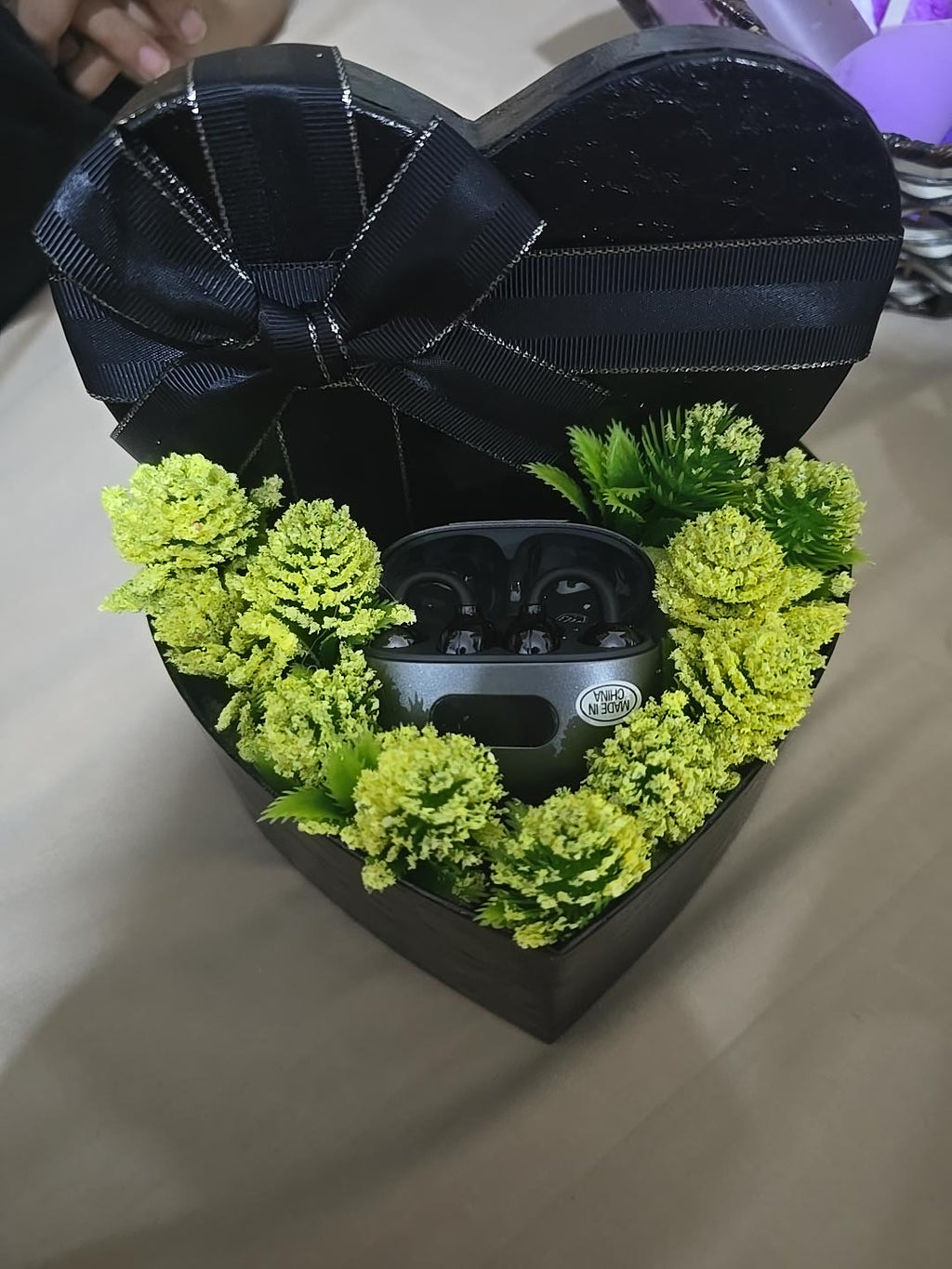 BioCode wireless Bluetooth earbuds in a metallic charging case nestled inside a black heart-shaped gift box with greenery