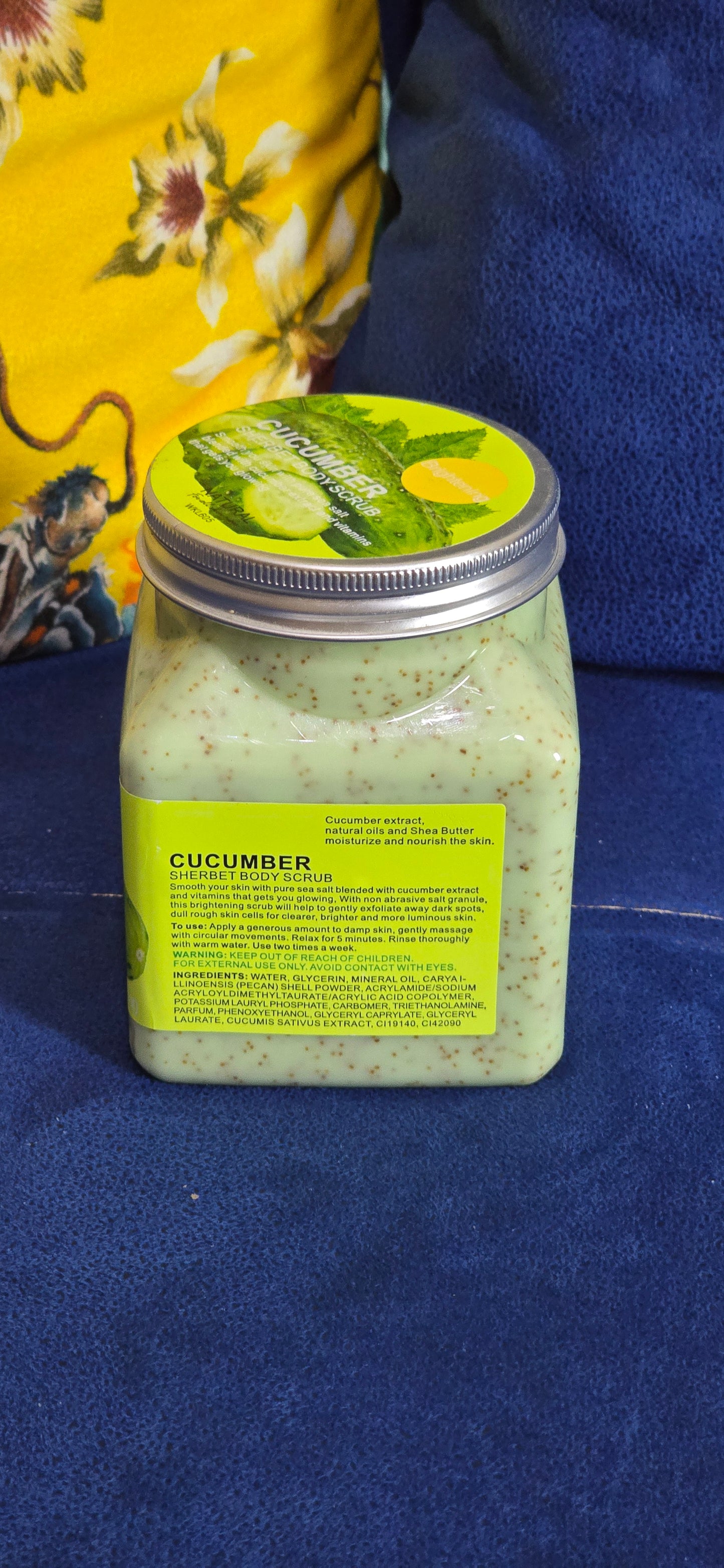 A jar of cucumber spread with a green and yellow label, resting on a dark blue textured fabric next to a yellow floral cloth.